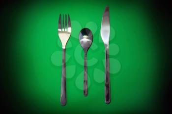 Table serving-knife,plate,fork on  green colour background.