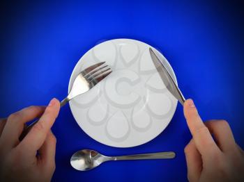 Table serving-knife, fork in hands on blue background.