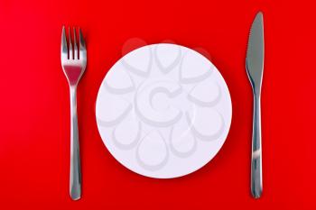 Table serving-knife,plate,fork on  red colour background.