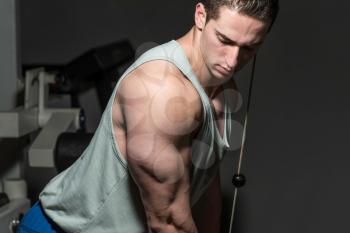 young bodybuilder doing heavy weight exercise for triceps with cable