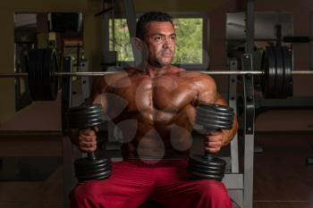 shirtless body builder posing with dumbbell at the bench