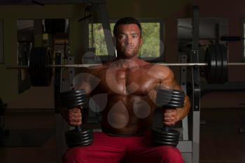 shirtless body builder posing with dumbbell at the bench