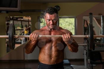 bodybuilder doing heavy weight exercise for biceps with barbell