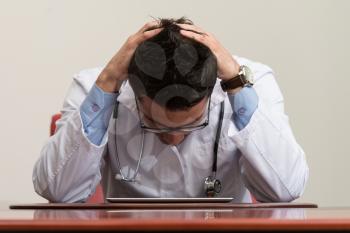 Stressed Out Doctor With Hands Clasped Sitting At Table In Conference Room