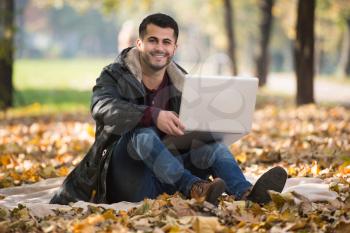 Handsome Man Working On Laptop In Park During Autumn Season