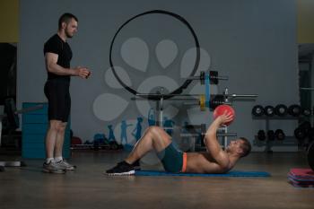 Young Man With Personal Trainer Doing Medicine Ball Exercises