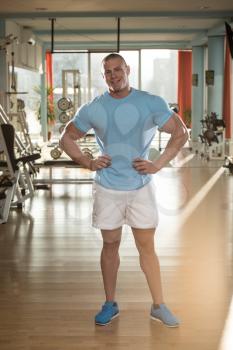 Serious Man Standing In The Gym And Flexing Muscles In T-Shirt