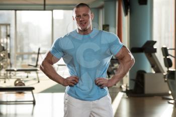 Serious Man Standing In The Gym And Flexing Muscles In T-Shirt