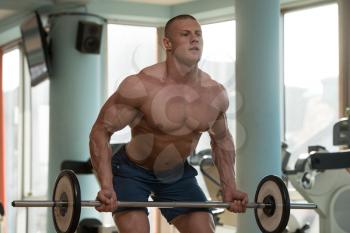 Young Muscular Man Doing Heavy Weight Exercise For Back With Barbell