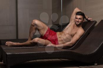 Young Man Resting On Sun Loungers By Swimming Pool And Flexing Muscles