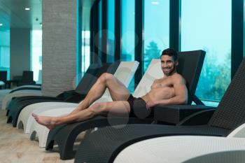 Young Man Resting On Sun Loungers By Swimming Pool And Flexing Muscles