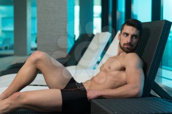 Young Man Resting On Sun Loungers By Swimming Pool And Flexing Muscles