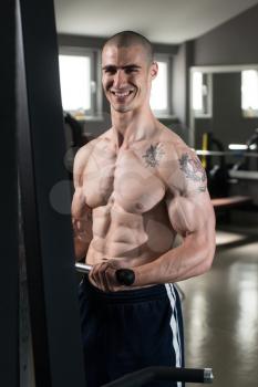 Young Muscular Fitness Bodybuilder Doing Heavy Weight Exercise For Biceps On Machine With Cable  In The Gym