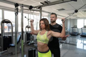 Personal Trainer Showing Young Woman How To Train Biceps On Machine In The Gym