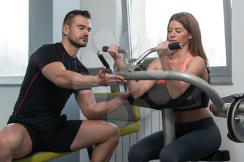 Personal Trainer Showing Young Woman How To Train Biceps On Machine In The Gym