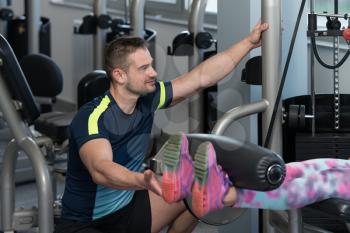 Personal Trainer Showing Young Woman How To Train Legs On Machine In The Gym