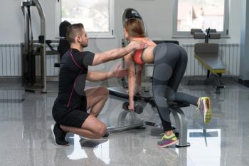 Personal Trainer Showing Young Woman How To Train Back Exercise With Dumbbell In A Health And Fitness Concept