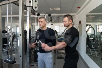 Personal Trainer Showing Young Man How To Train Triceps On Machine In The Gym