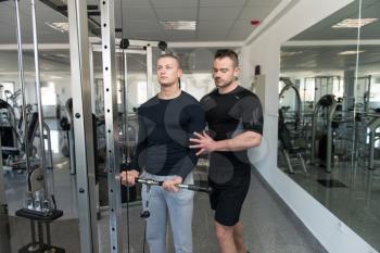 Personal Trainer Showing Young Man How To Train Biceps On Machine In The Gym
