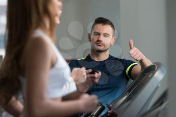 Personal Trainer Showing Ok Sign To Client - Group Of People Exercising On Treadmills In Gym Or Fitness Club