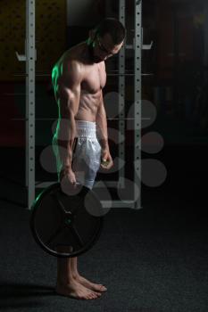 Portrait Of A Physically Young Man Holding Weights In Hand In A Dark Gym