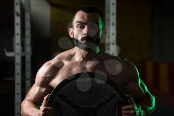 Portrait Of A Physically Young Man Holding Weights In Hand In A Dark Gym