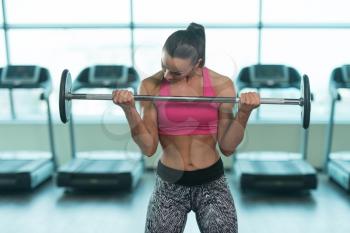 Young Woman Exercising Biceps With Barbell In The Gym And Flexing Muscles - Muscular Athletic Bodybuilder Fitness Model