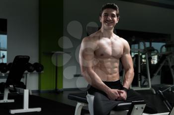 Good Looking And Attractive Young Man With Muscular Body Sitting On Bench And Relaxing In Gym
