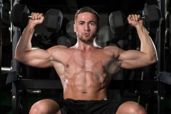 Young Strong Man In The Gym And Exercising Shoulders With Dumbbells - Muscular Athletic Bodybuilder Fitness Model Exercise Shoulder