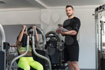 Personal Trainer Showing Young Woman How To Train Chest On Machine In The Gym