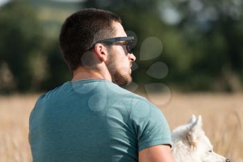 Young Man Sitting With Dog German Spitz In Harvested Field