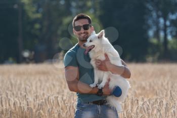 Young Man Standing With Dog German Spitz In Harvested Field