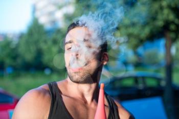 Young Man Smoking Shisha Outdoors - Man Exhaling Smoke Inhaling From A Hookah