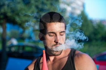 Young Man Smoking Shisha Outdoors - Man Exhaling Smoke Inhaling From A Hookah