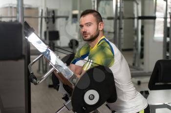 Attractive Man Doing Heavy Weight Exercise For Biceps On Machine In A Gym