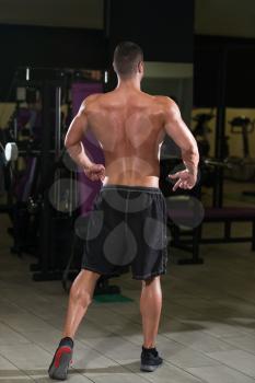 Young Man Standing Strong In The Gym And Flexing Rear Lat Spread Pose - Muscular Athletic Bodybuilder Fitness Model Posing Exercises