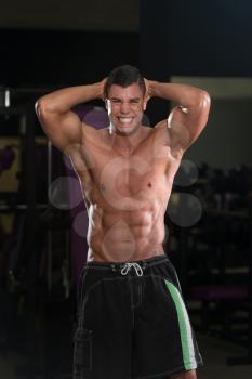 Young Man Standing Strong In The Gym And Flexing Muscles - Muscular Athletic Bodybuilder Fitness Model Posing Showing Abs After Exercises