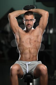 Handsome Man Wearing Glasses Working Out Triceps With Dumbbell In A Dark Gym