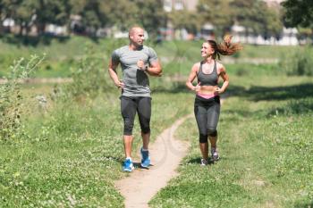 Young Couple Running In Wooded Forest Area - Training And Exercising For Trail Run Marathon Endurance - Fitness Healthy Lifestyle Concept