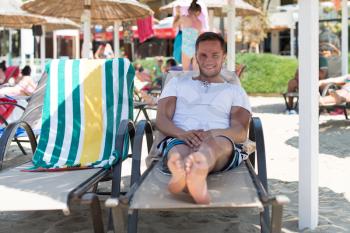 Portrait of Handsome Happy Smiling Man Lying on Chair on Beach by Sea