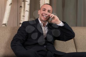 Young Happy Man Sitting Relaxed on Sofa and Talking on the Phone