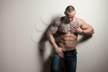 Portrait of a Tattoo Man In Jeans Showing His Abs Standing Isolated on Gray Background