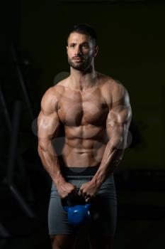 Young Man Working Out With Kettle Bell In A Dark Gym - Bodybuilder Doing Heavy Weight Exercise With Kettle-bell