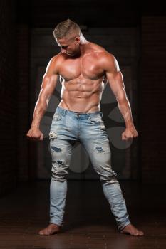 Healthy Young Man In Jeans Standing Strong In The Gym And Flexing Muscles - Muscular Athletic Bodybuilder Fitness Model Posing After Exercises