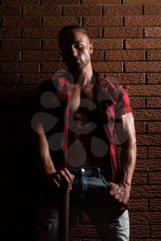 Healthy Young Man Standing Strong In The Gym And Flexing Muscles While Wearing Plaid Shirt - Muscular Athletic Bodybuilder Fitness Model Posing After Exercises On Wall of Bricks