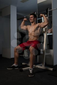 Handsome Man Sitting Strong In The Gym And Flexing Muscles - Muscular Athletic Bodybuilder Fitness Model Posing After Exercises