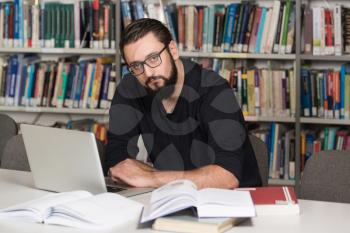 In The Library - Handsome Male Student With Laptop And Books Working In A High School - University Library - Shallow Depth Of Field