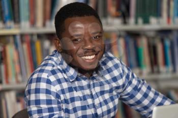 Portrait Of African Clever Student With Open Book Reading It In College Library - Shallow Depth Of Field