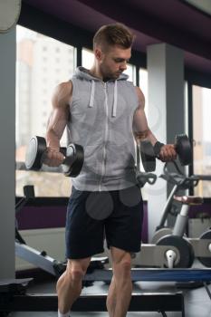 Muscular Young Man Doing Heavy Weight Exercise For Biceps With Dumbbells In Modern Fitness Center Gym