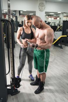 Personal Trainer Showing Young Woman How To Train Biceps In The Gym